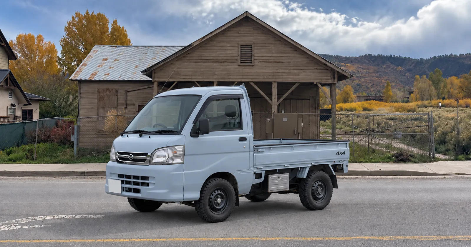 Illustration of a pale blue Daihatsu Hijet truck on a street in front of an old wooden creamery building, autumn hills behind
